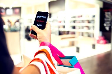 Close up of man's hand holding shopping bags and smartphone with shopping online inscription.