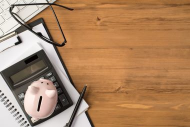 photo of keyboard calculator, notebook, clipboard pen, piggybank, and glasses isolated on wooden backdrop.